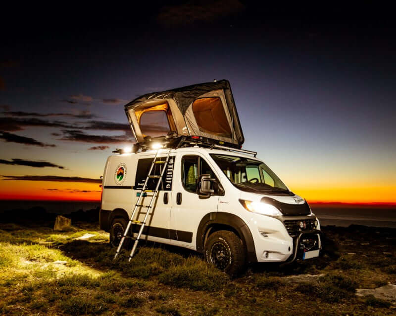 Furgone con tenda da tetto Wild Land aperta e scala appoggiata al tramonto