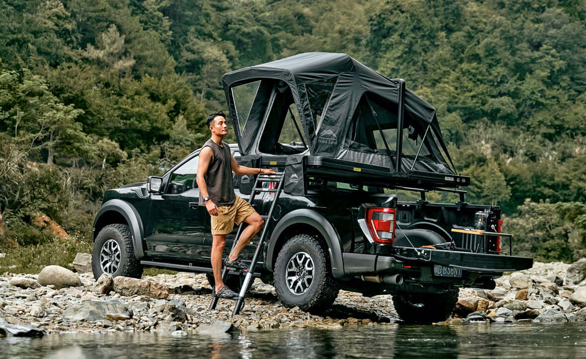 Pick-up con tenda da tetto Wild Land aperta sul cassone accanto a un torrente