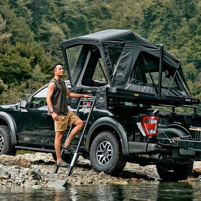 Pick-up con tenda da tetto Wild Land aperta sul cassone accanto a un torrente