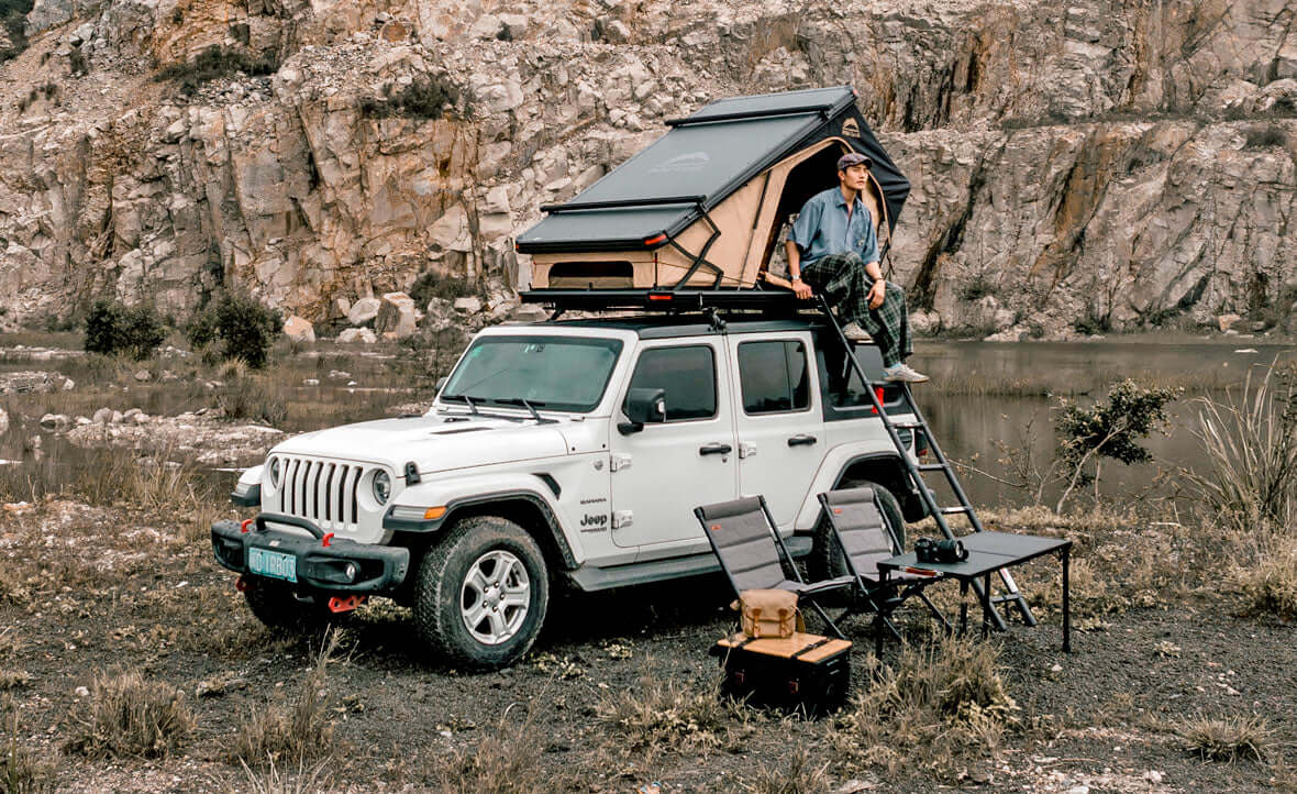 Jeep Wrangler bianca con tenda da tetto Wild Land aperta e campo tra le rocce