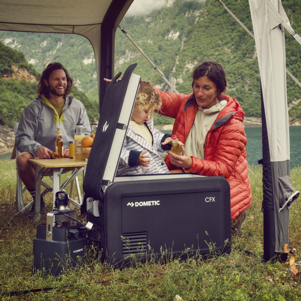 Famiglia al campo sotto una veranda con un frigorifero portatile Dometic CFX aperto