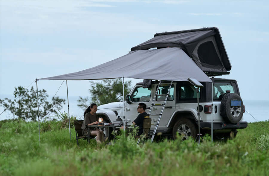Jeep Wrangler con tenda da tetto e tendalino Wild Land aperto su un prato