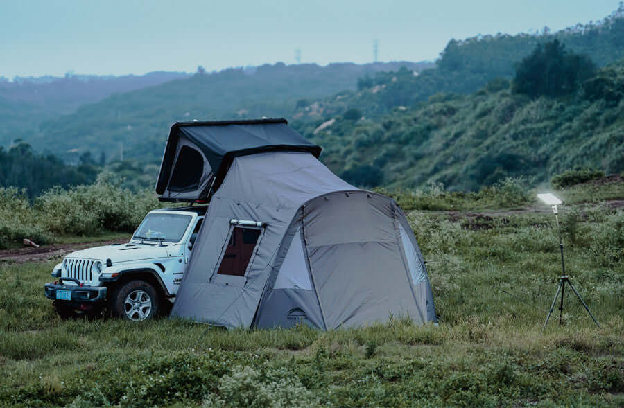 Jeep con tenda da tetto Wild Land e tendalino con pareti montato su un prato di collina