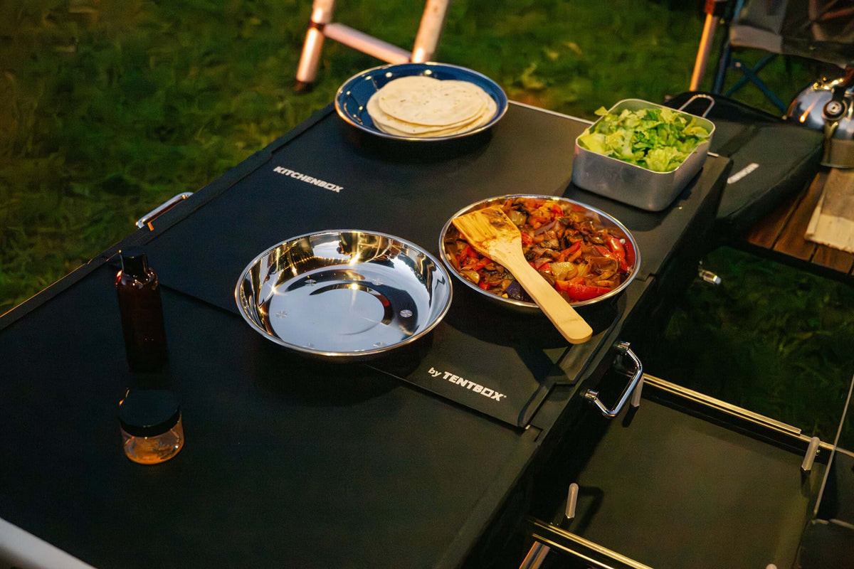 Piano di una cucina da campo TentBox con piatti in acciaio, verdure e fajitas