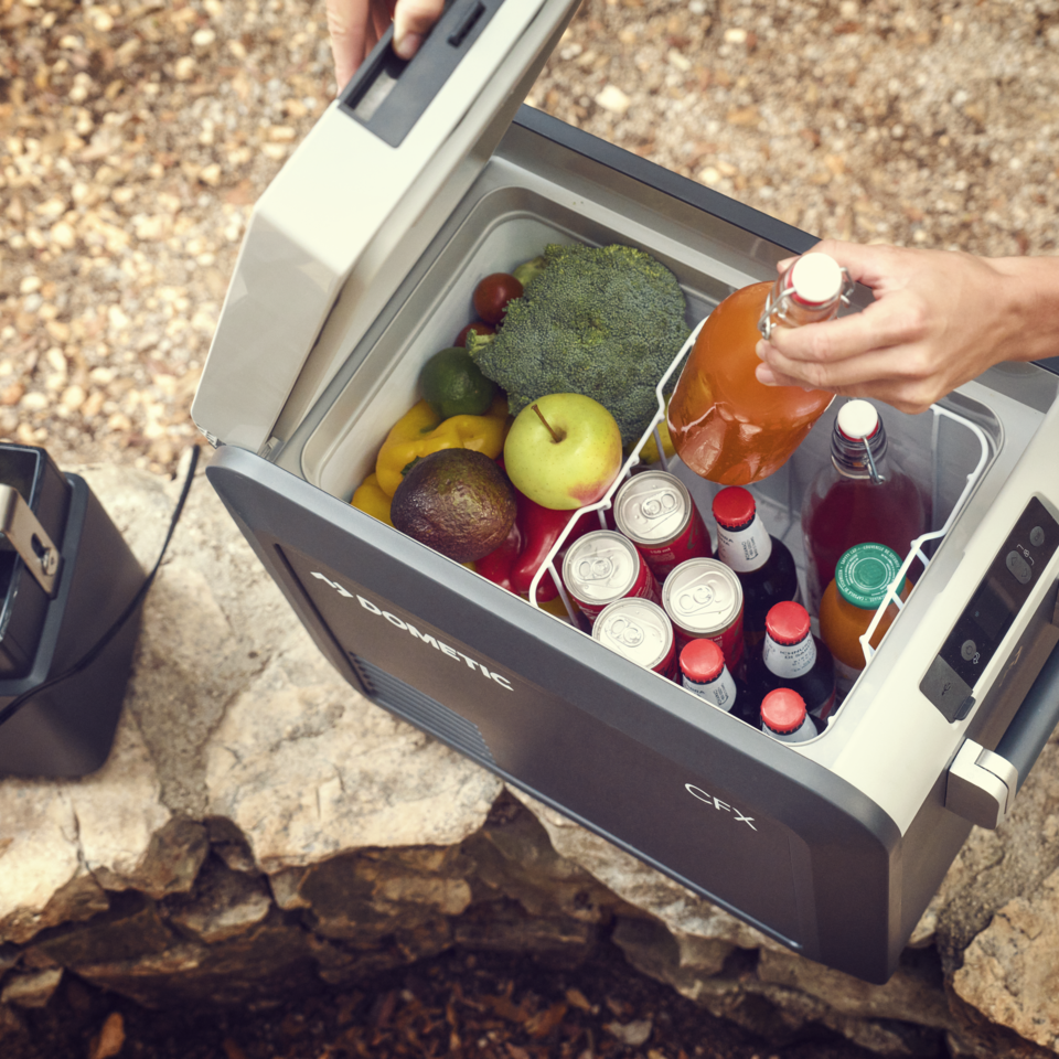 Frigorifero portatile Dometic aperto con frutta e bibite accanto a una power station